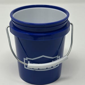 May include: A small, cylindrical blue plastic bucket with a white interior lining. It features a silver metal wire handle with a white plastic grip. The front of the bucket displays a white graphic logo with the text Lowe's in a stylized font.