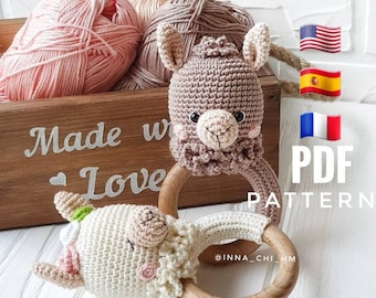 May include: A handmade crochet llama and sheep baby rattle with wooden rings. The llama is light brown and the sheep is white. The rattles are displayed with pink, beige, and brown yarn in a wooden box that says "Made with Love".