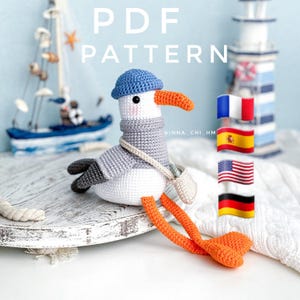 May include: Crochet pattern PDF for a cute amigurumi seagull wearing a blue hat and a grey scarf. The pattern includes instructions for making the seagull in multiple languages, including French, Spanish, German, and English.