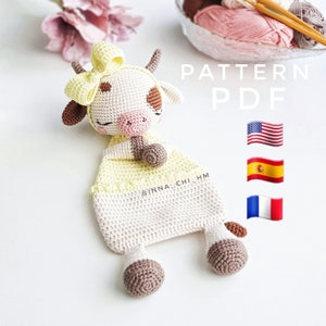 Könnte beinhalten: Häkelanleitung für Amigurumi-Kuh im PDF-Format in Englisch, Spanisch und Französisch. Die Anleitung enthält Anweisungen zum Häkeln einer Kuh mit einer gelben Schleife, braunen Flecken und einer rosa Nase. Die Anleitung steht als PDF-Datei zum Download bereit.