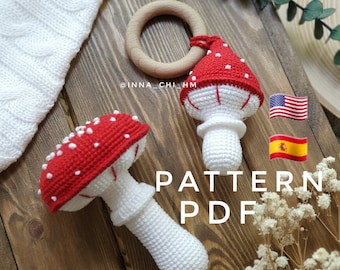 May include: Crochet pattern for a red and white mushroom baby toy with a wooden ring. The pattern is available in English and Spanish. The text "PATTERN PDF" is written in white on a wooden background.