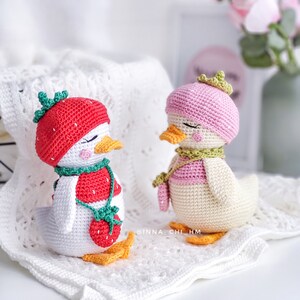 Peut inclure: Deux figurines de canard crochet&eacute;es &agrave; la main. L'un porte un chapeau fraise rouge et un bavoir assorti avec un pendentif fraise. L'autre porte un b&eacute;ret et une &eacute;charpe roses avec une petite couronne. Les deux ont les yeux ferm&eacute;s et des becs oranges.