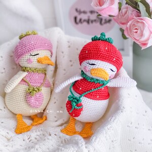 Peut inclure: Deux poup&eacute;es canard faites &agrave; la main au crochet. L'une porte un b&eacute;ret rose, un haut rose et blanc et un sac &agrave; main fraise. L'autre porte un chapeau fraise rouge, un haut rouge et blanc et un sac &agrave; main fraise. Les deux ont des becs et des pieds oranges.