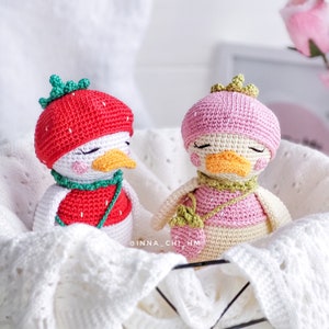 Peut inclure: Deux poup&eacute;es canards crochet&eacute;es &agrave; la main dans un panier blanc. L'un porte un chapeau et un gilet fraise rouges. L'autre a un chapeau et un gilet roses, avec un petit sac &agrave; main fraise. Les deux ont les yeux ferm&eacute;s et un bec orange.