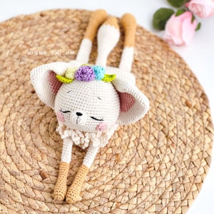 May include: A crocheted white bunny with long legs and a flower crown. The bunny is lying on a woven straw mat.
