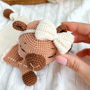 May include: A crocheted brown and white animal toy with a white bow. The toy has a brown nose and closed eyes.