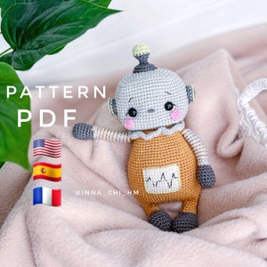 Può includere: Schema a crochet PDF per un adorabile robot amigurumi. Il robot è grigio con accenti arancioni e ha un'espressione dolce. Lo schema è disponibile in inglese, spagnolo e francese.