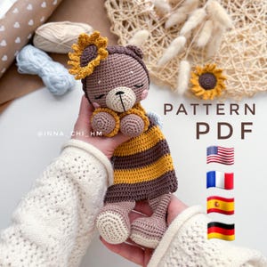 以下が含まれることがあります： 頭の上にひまわりをつけた、茶色と黄色のミツバチをテーマにしたテディベアのための、かぎ針編みのパターンPDF。パターンは英語、フランス語、スペイン語、ドイツ語で入手できます。