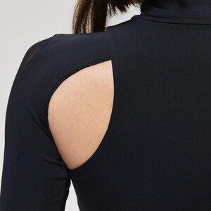 May include: Black long-sleeve top with a high neckline and a cutout detail on the shoulder. The top is made of a smooth, stretchy fabric. The cutout reveals a portion of the shoulder and upper arm.
