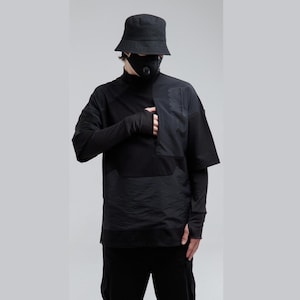 May include: Black layered top with short sleeves and a high collar, worn with black trousers and a bucket hat. The top has a textured panel and long sleeves with fingerless gloves. A black face mask is also worn.
