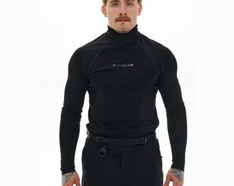 May include: A black long-sleeve mock neck shirt featuring the text "TUP WEAR" in small grey letters on the chest. The shirt has a fitted design with visible seam detailing across the shoulders and chest, paired with black pants featuring a belt.