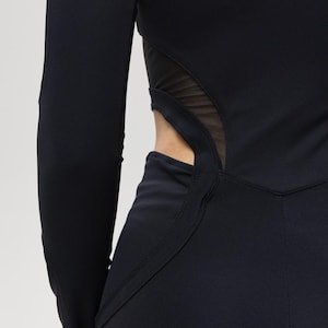 May include: Black long-sleeved athletic wear with a mesh panel detail at the waist. The garment has a form-fitting design with a high neckline and a streamlined silhouette, suitable for active pursuits.