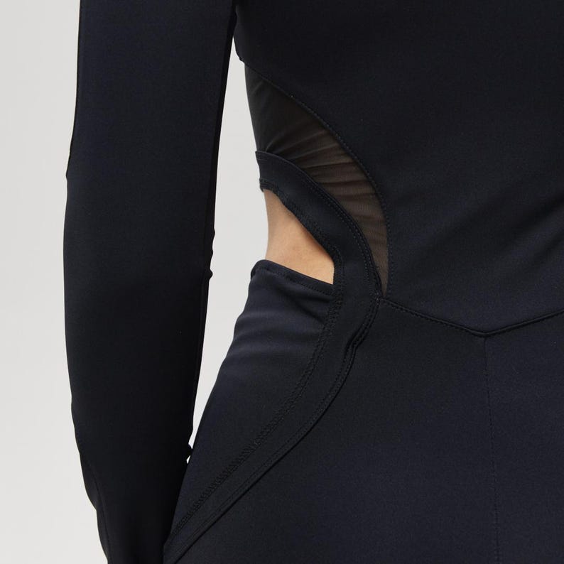 May include: Black long-sleeved athletic wear with a mesh panel detail at the waist. The garment has a form-fitting design with a high neckline and a streamlined silhouette, suitable for active pursuits.