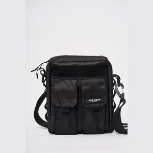 May include: Black crossbody bag with two front pockets and a velcro patch. The bag has a shoulder strap and a carabiner clip. The text "TUR WEAR" is visible on the front of the bag.