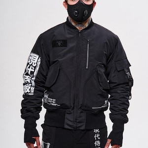 May include: Black bomber jacket with multiple pockets, a zip closure, and Japanese text on the sleeve and pants. The jacket features a small patch on the chest and is paired with black pants. A black face mask is also visible.