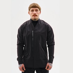 Könnte beinhalten: Schwarze Langarmjacke mit hohem Kragen und durchgehendem Reißverschluss. Die Jacke hat ein minimalistisches Design mit einer einzelnen Brusttasche. Das Model trägt einen schwarzen Rollkragenpullover darunter.