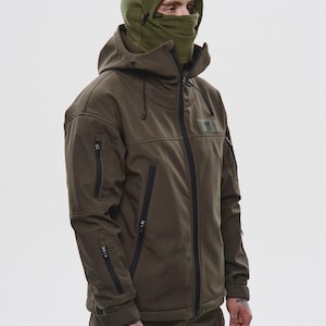 May include: Olive green hooded jacket with black zippers and multiple pockets. The jacket features a matching olive green balaclava. The model is wearing olive green pants. The jacket has a patch on the upper chest.