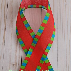 May include: Red ribbon with green and blue stripes. The ribbon is folded in half and the stripes are visible on both sides.
