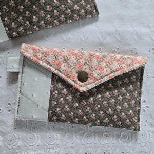 May include: Two small, quilted fabric wallets. One wallet is open, revealing a light green section. The wallets feature a floral pattern in pink and white on a dark gray background. Each wallet has a snap closure.