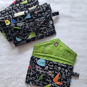 May include: Black fabric wallets with a math-themed design. The wallets feature equations, geometric shapes, and the text "Matrix Multiplication" and "Integers" in white. The interior lining of one wallet is bright green with a circuit board pattern.
