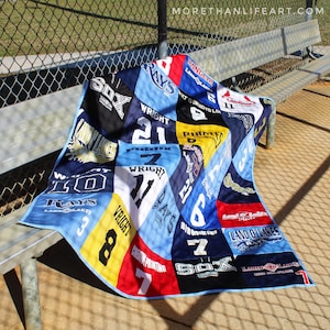 May include: A patchwork quilt constructed from various sports jerseys in shades of blue, black, yellow, red, and white. The quilt features numerous printed team names, player numbers, and corporate logos, including Rays, Sox, Cardinals, and Land O' Lakes.