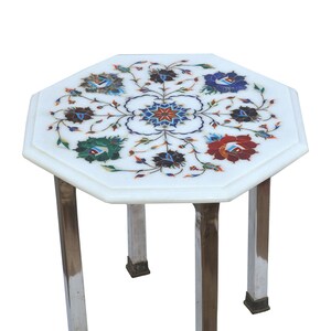 May include: White marble side table with an octagonal top. The tabletop features a floral mosaic design in shades of blue, red, green, and brown. The table has four polished metal legs.