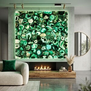 May include: A large, rectangular wall art piece composed of green and white agate stones. The stones are backlit, creating a glowing effect. The artwork is mounted above a fireplace with a modern design, and a beige sofa with a green pillow is in the foreground.