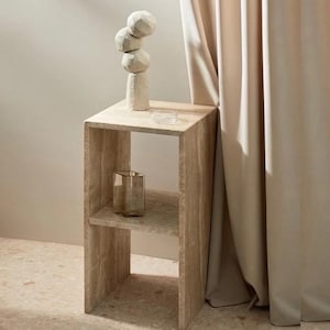 May include: A light brown wooden side table with two shelves. The table has a simple, modern design and is perfect for a small space. A white ceramic sculpture sits on the top shelf.