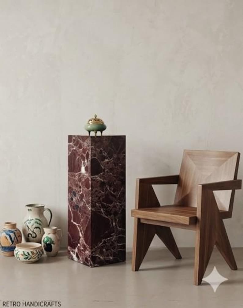 May include: A wooden chair with geometric design and a tall, rectangular marble pedestal with a small green and gold decorative object on top. Several ceramic vases with painted designs are on the left.