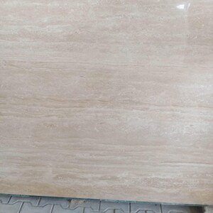 May include: A large, rectangular slab of beige stone with a polished surface. The stone has a natural, flowing grain pattern with subtle variations in color, creating a warm and inviting aesthetic. The stone is likely a countertop or flooring material.