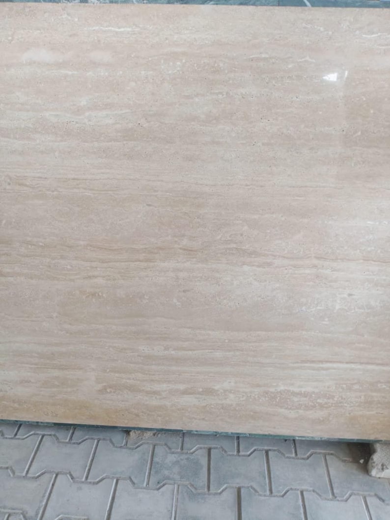 May include: A large, rectangular slab of beige stone with a polished surface. The stone has a natural, flowing grain pattern with subtle variations in color, creating a warm and inviting aesthetic. The stone is likely a countertop or flooring material.