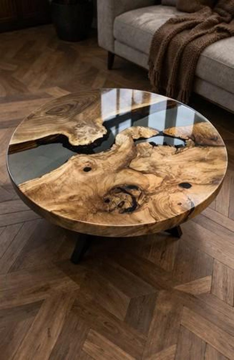May include: A round coffee table with a unique wood grain design and a glossy, clear resin finish. The table has a dark, natural wood colour with black legs. The table's diameter is approximately 100 cm.