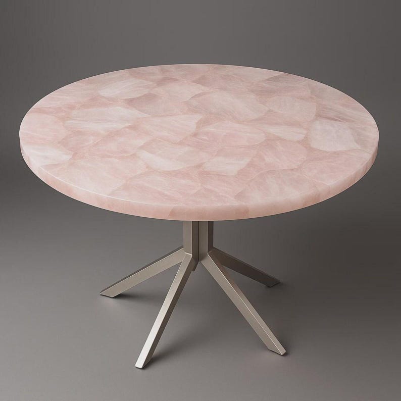 K&ouml;nnte beinhalten: Ein runder Tisch mit einer rosa, mosaikartigen Tischplatte und einem Gestell aus geb&uuml;rstetem Metall. Die Tischplatte besteht aus einem hellrosa Material mit einem Muster aus unregelm&auml;&szlig;igen Formen. Das Gestell hat ein sternf&ouml;rmiges Design mit vier Beinen.