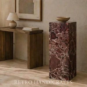 May include: A dark wooden console table with a small lamp and books, and a tall, rectangular marble pedestal with a bowl on top. The pedestal is a deep red color with white veining. The text "RETRO HANDICRAFTS" is at the bottom.