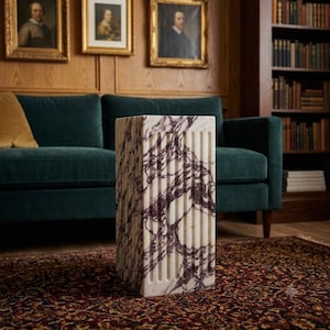 May include: A rectangular pedestal made of white marble with prominent purple veining. The structure features a fluted design on its vertical sides, creating a series of parallel grooves that run from the top to the bottom of the piece.