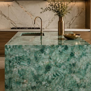 May include: A modern kitchen island with a vibrant green, mosaic-like countertop. A gold faucet and a brass vase with greenery add elegance. The background features a marble backsplash and wooden cabinetry, creating a luxurious aesthetic.