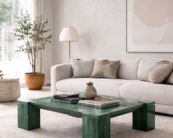 May include: A living room with a green marble coffee table, books, and a vase. A white sofa with neutral cushions is against a textured wall. A floor lamp and a potted plant enhance the room's decor. The coffee table is approximately 120 cm long.