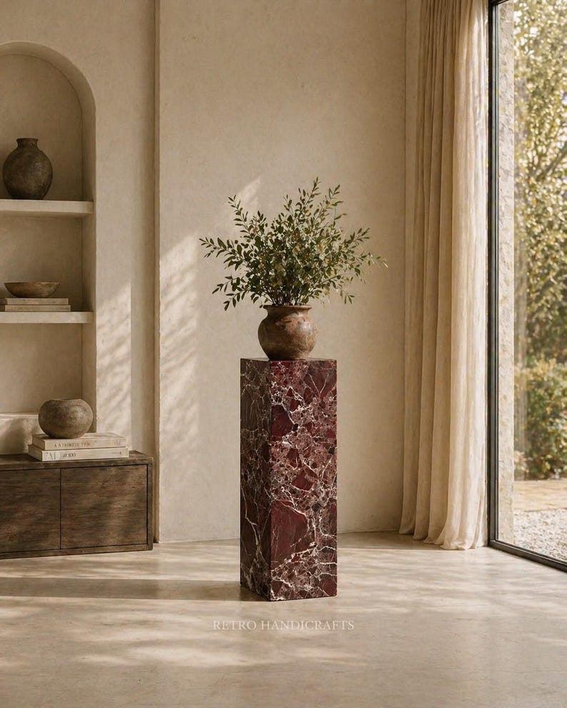 May include: A tall, rectangular marble pedestal with a rich burgundy and white veined pattern. A brown ceramic vase filled with green foliage sits atop the pedestal. The text "RETRO HANDICRAFTS" is at the bottom.