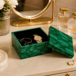 May include: An open green malachite jewellery box with a black velvet interior, containing a gold watch, a gold bracelet, and a ring. A gold watch is visible. The box is open.