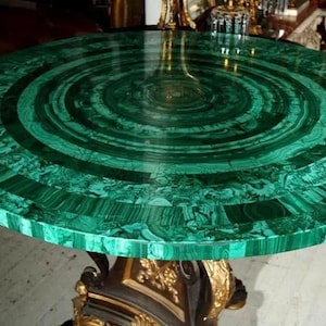 May include: A round table with a malachite top, featuring concentric circles of deep green hues. The table's base is ornate, with gold and brown accents. This decorative table is a statement piece for any living space.