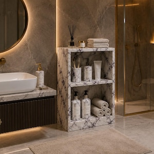 Puede incluir: Una estantería de baño de mármol blanco de dos niveles con vetas negras. Los estantes contienen un soporte para cepillos de dientes, dispensadores de jabón, un tubo de crema y toallas enrolladas en un baño con lavabo y espejo.