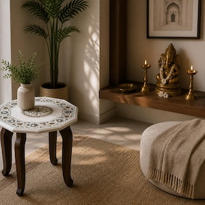 May include: An octagonal side table with a white and patterned top and dark brown legs. A beige vase with greenery sits on the table. The room also features a decorative statue, candles, and a beige ottoman.