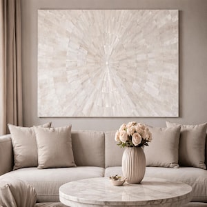May include: A neutral-toned living room featuring a large, abstract wall art piece with a radial design. A beige sofa with matching pillows is in front of the art. A round marble coffee table and a vase of roses complete the scene.