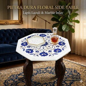 May include: Pietra Dura floral side table with Lapis Lazuli and marble inlay. The white tabletop features a blue floral design and rests on dark wooden legs. A decorative tray and a glass bottle are on the table. The table is approximately 24 inches in diameter.