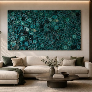 May include: A large, rectangular teal and black abstract art piece hangs above a cream-colored sectional sofa. The artwork features a pattern of circular shapes. The living room has a modern design with a round coffee table and decorative pillows.