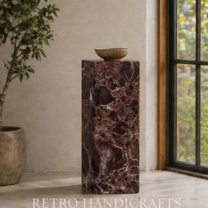 May include: A rectangular, maroon marble pedestal with white veining, topped with a small, round, light brown bowl. The pedestal is in front of a window and the text "RETRO HANDICRAFTS" is at the bottom.
