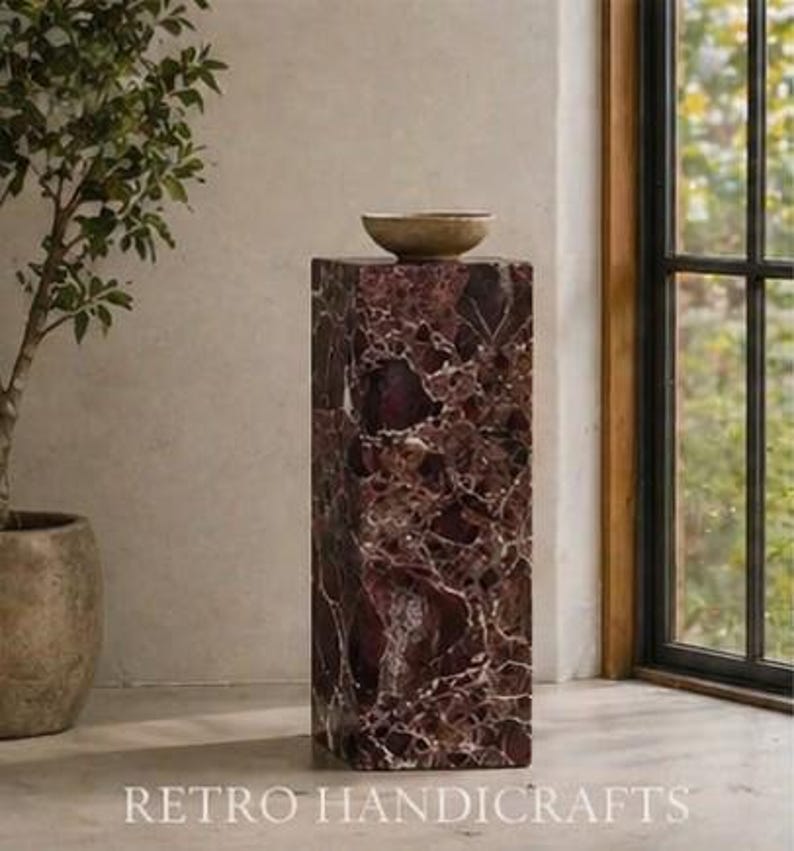 May include: A rectangular, maroon marble pedestal with white veining, topped with a small, round, light brown bowl. The pedestal is in front of a window and the text "RETRO HANDICRAFTS" is at the bottom.
