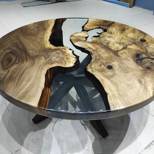May include: A circular coffee table with a distinctive design. The tabletop is crafted from light brown wood, featuring dark brown and clear resin details. The table is supported by a dark brown base with four legs.