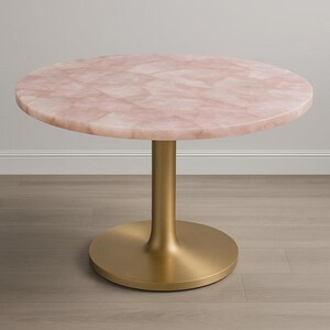 K&ouml;nnte beinhalten: Ein runder Tisch mit einer rosa, mosaikartigen Tischplatte und einem goldfarbenen Sockel. Der Tisch steht auf einem hellen Holzboden. Das Design des Tisches ist modern und elegant.