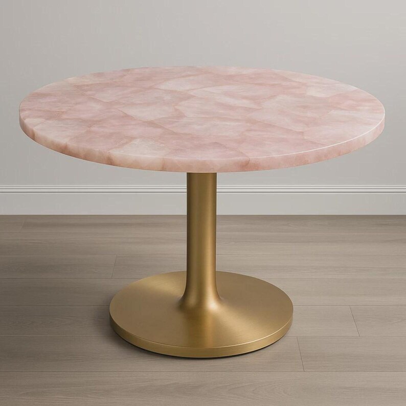 K&ouml;nnte beinhalten: Ein runder Tisch mit einer rosa, mosaikartigen Tischplatte und einem goldfarbenen Sockel. Der Tisch steht auf einem hellen Holzboden. Das Design des Tisches ist modern und elegant.